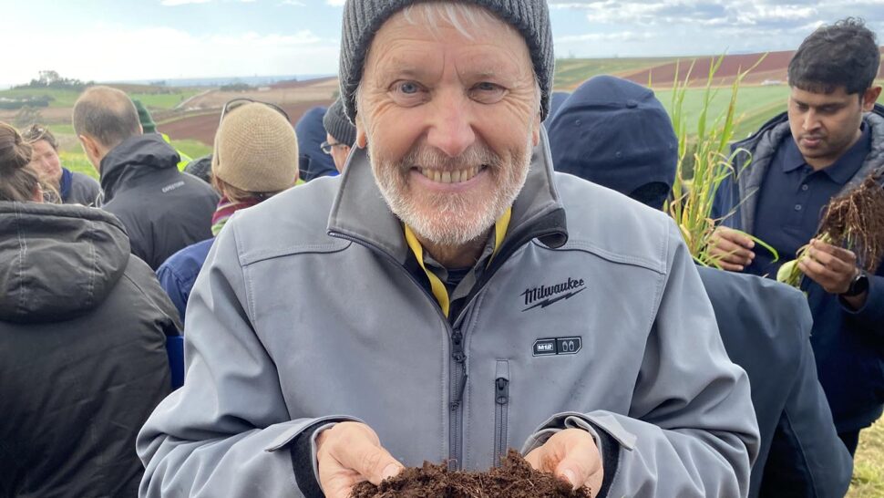 Soil CRC Program 2 Leader, Dr Richard Doyle, stands in a field site holding soil and looking to camera with a smile on his face.