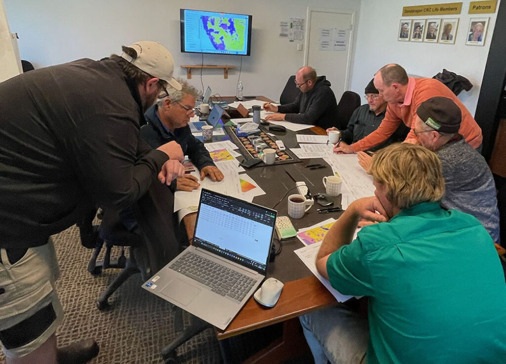 Two of the project team members assist a small group of farmers and advisors who are sitting around a table and working through activities.